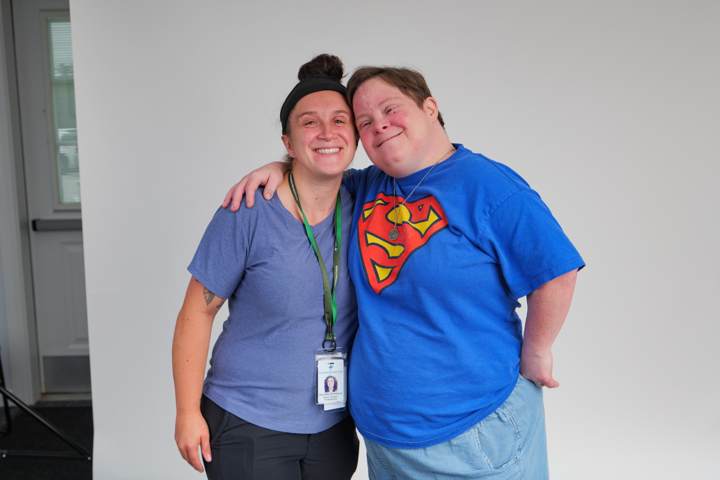 A staff member and a young man in a superhero shirt smile with arms around each other